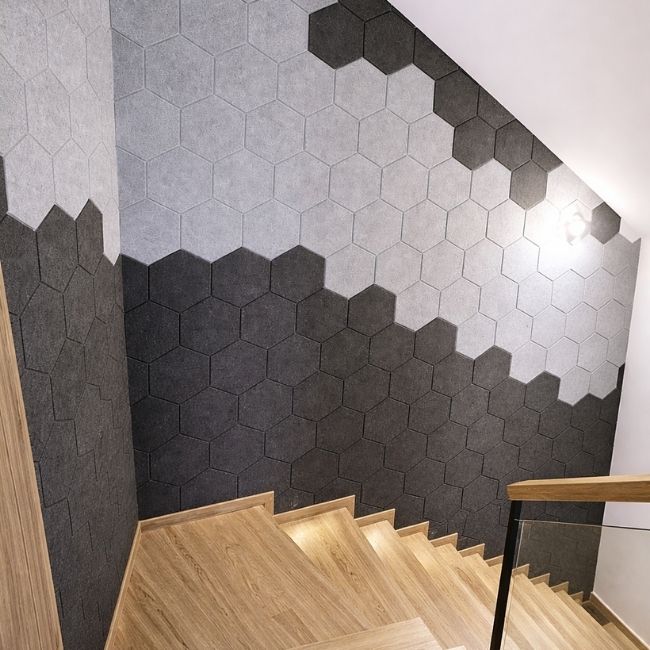 Hexagonal tiles in black and gray on a wall with wooden stairs.